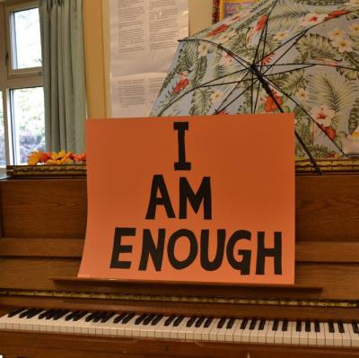 Sign saying I AM ENOUGH in black letters on orange background sitting on a piano