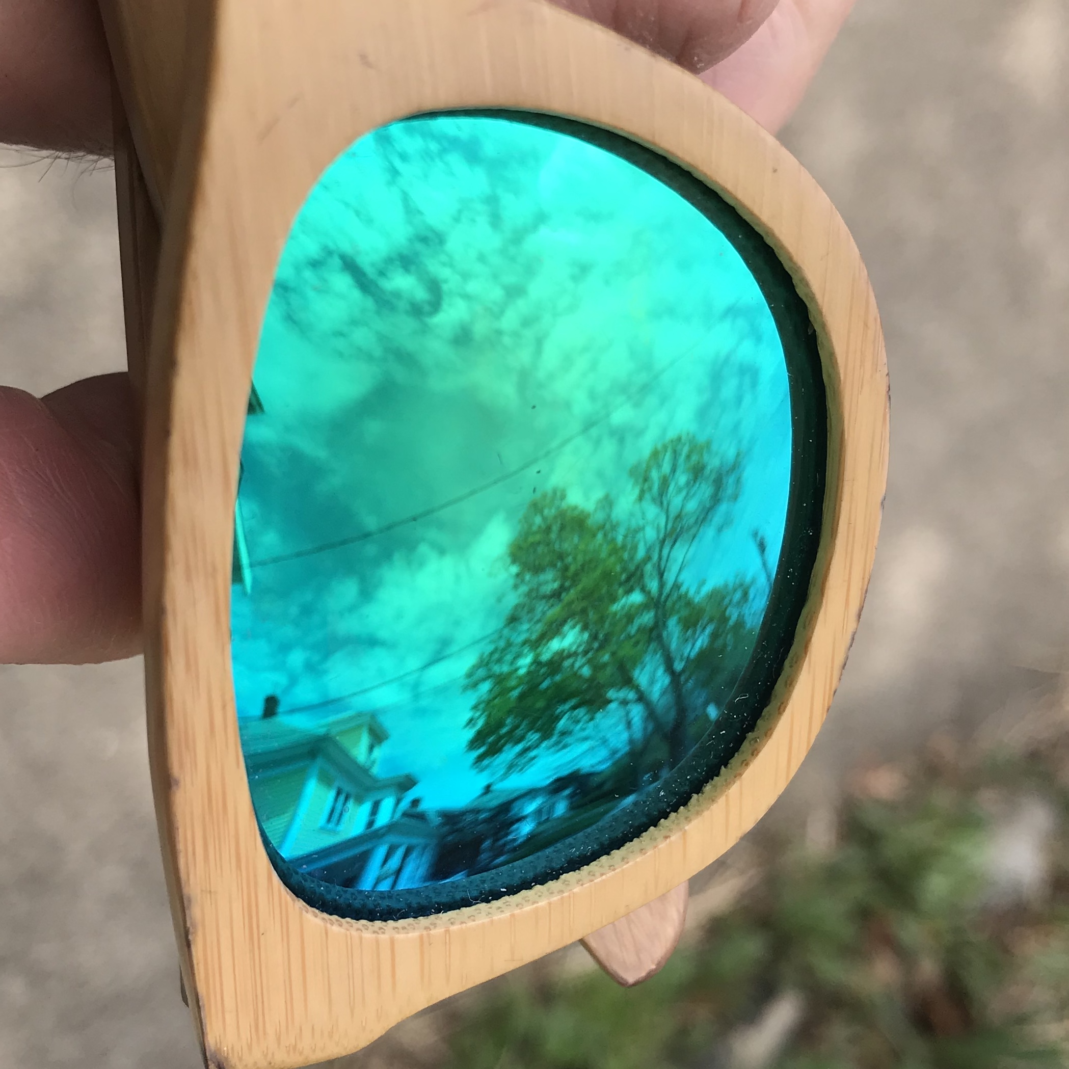 sunglasses with reflective lenses reflecting the sky, a tree, and a house